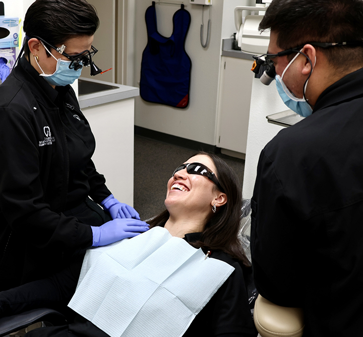 Two dental professionals talking to a woman in the dental chair