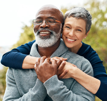 Senior woman hugging senior man from behind