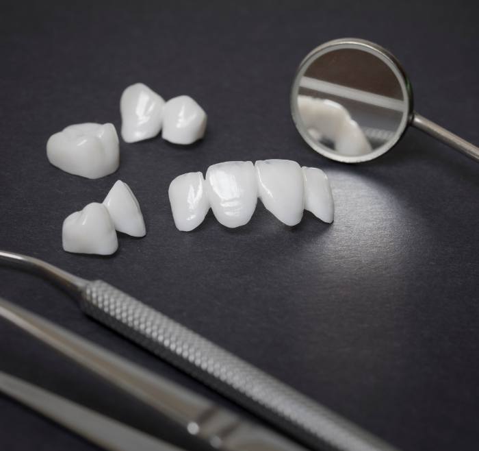 Several white dental crowns and veneers next to dental instruments