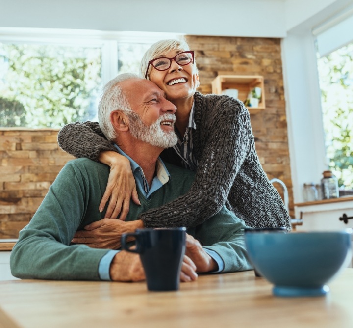 Senior couple at their kitchen table smiling with dental implants in San Antonio