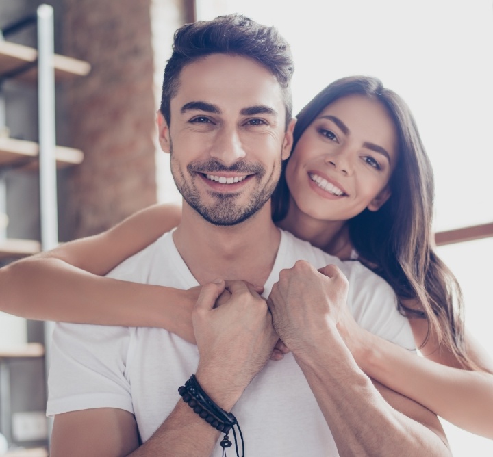 Young woman hugging young man from behind and smiling after dental services in San Antonio