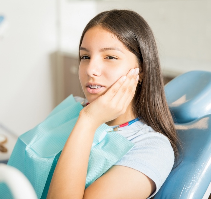 Young woman holding her cheek in pain while sitting in dental chair