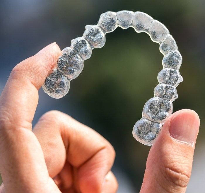 Close up of a hand holding a Sure Smile clear aligner