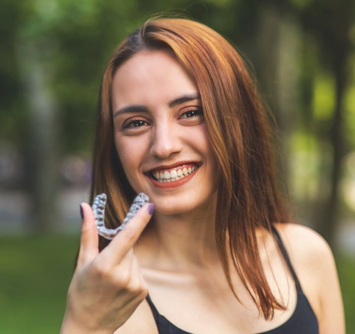 Smiling young woman holding a clear aligner outdoors