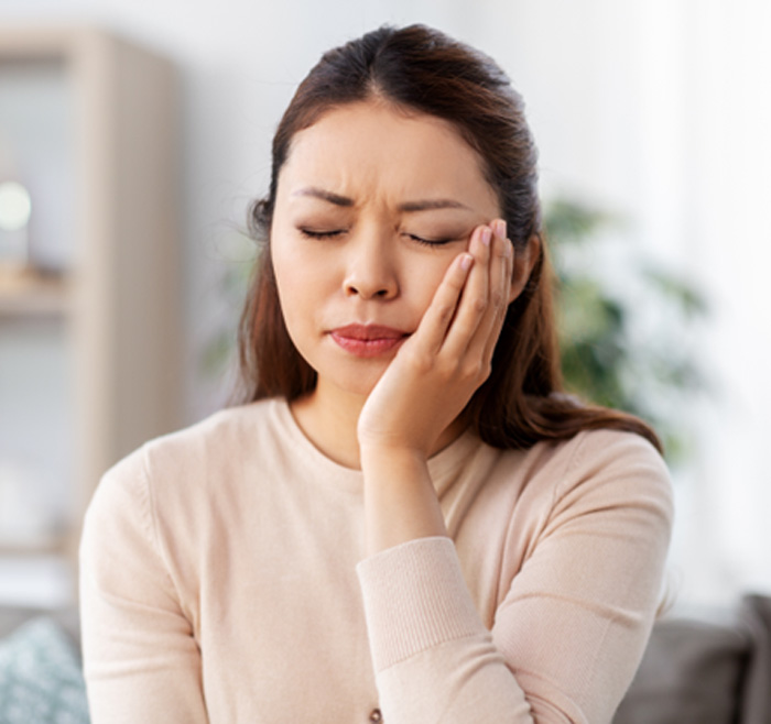 Young woman holding her cheek in pain while sitting in dental chair