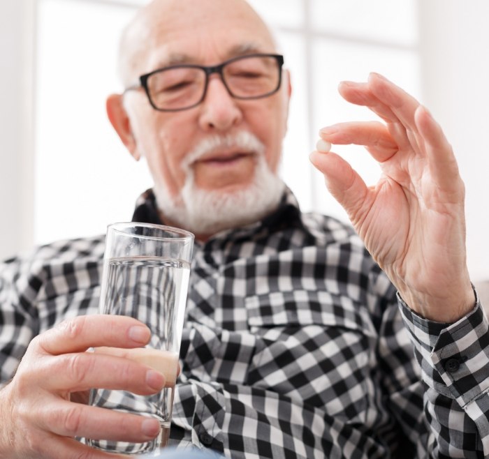 Senior man holding a pill and a glass of water