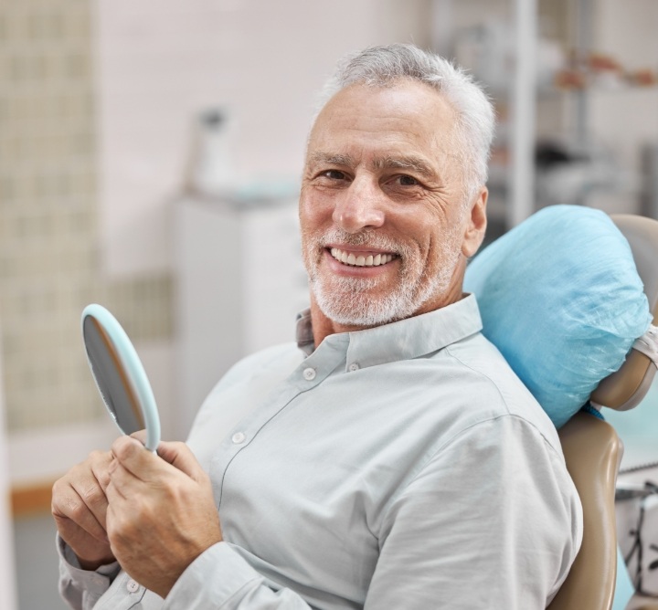 Smiling senior man sitting in dental chair and holding a mirror