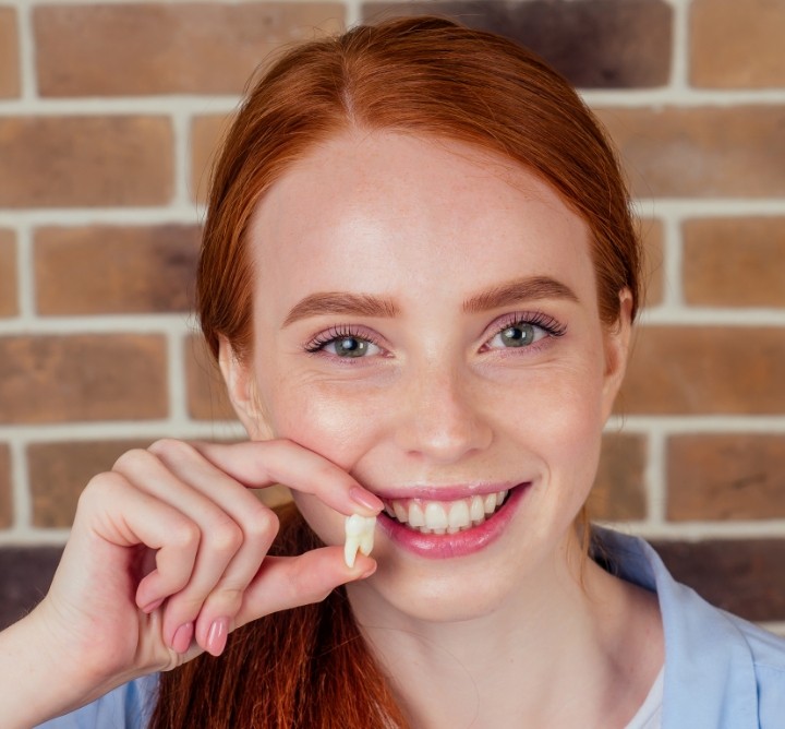 Smiling woman holding an extracted tooth