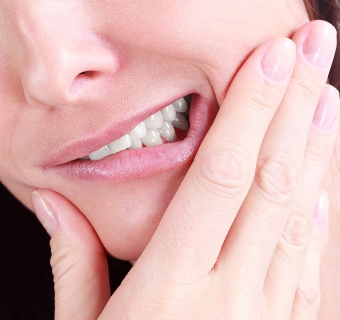 Close up of a person wincing and holding the side of their jaw