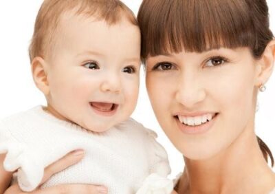 A smiling mother holds her joyful baby close, both looking directly at the camera.