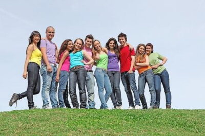 Group of ten young adults smiling together on a grassy hill under a clear sky.