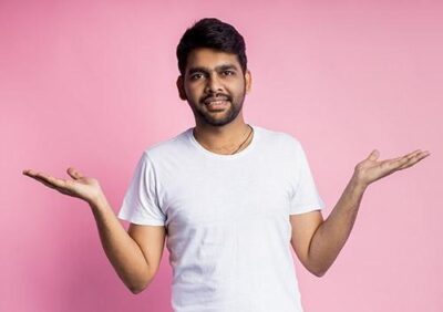 Young man in a white shirt smiles and raises his hands, set against a pink background.